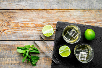 Alcoholic beverage. Whiskey with ice, mint and lime on black board on dark wooden background top view copy space