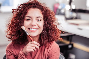Cheerful happy woman sitting with a makeup brush
