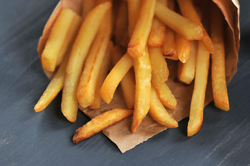 French fries in a packet of Kraft paper. Potatoes occupy the entire frame space. Dark background. Close-up. Macro shooting.