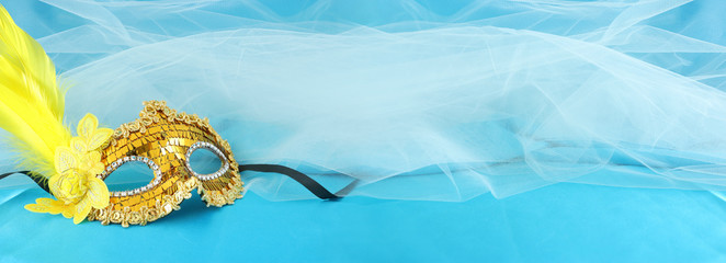 Banner of elegant and delicate gold venetian mask over turquoise silk and chiffon background.