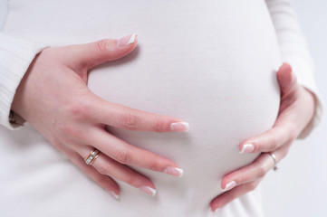 close up of pregnant belly in white woolen pullover with hands gently touching it
