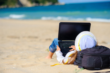 work in travel, girl teenager in a beach hat lies on the beach with a laptop