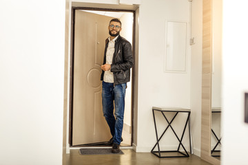 Handsome short-haired bearded man in a black jacket entering the apartment