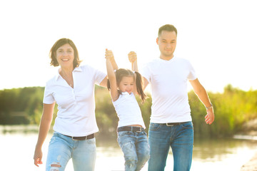 Fototapeta premium A happy family walks along the river bank on a sunny day, will barefoot on the water and splash, healthy outdoor recreation