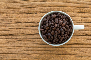 Top view a roasted coffee beans arranged in the cup coffee put on the vintage wood.