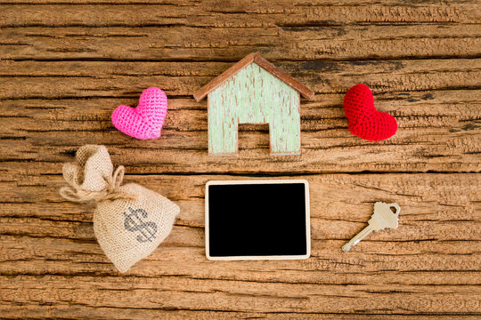 A wooden home and red heart for family and blackboard for ad text and house key and money bag put on the wood, Loan for real estate and advertising business concept.