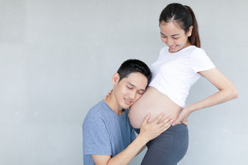 Fototapeta premium Lucky Asian man is listening to his beautiful pregnant wife's tummy and smiling.
