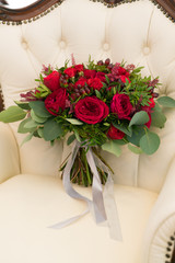 bright red wedding bouquet of fresh flowers and eucalyptus stands on the armchair