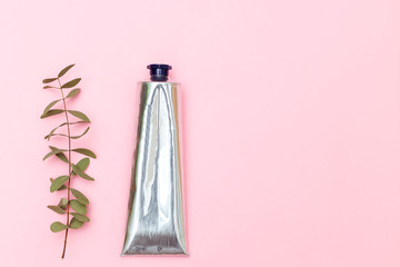Lotion in metal tube on pink background. Copy space
