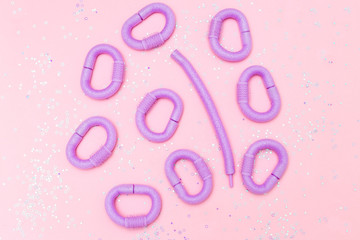 Violet hair curlers  and glitter on pink background. Flat lay