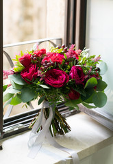 bright red wedding bouquet of fresh flowers and eucalyptus stands on the windowsill