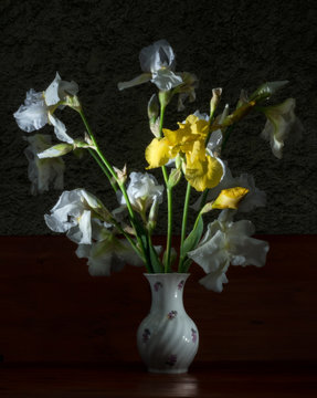 Bouquet of white and yellow irises in a vase on a dark background.