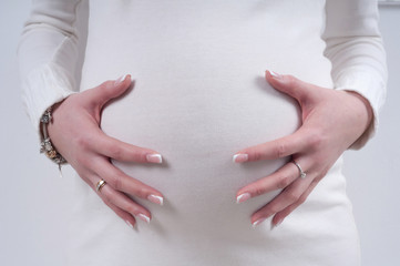 close up of pregnant belly in white woolen pullover with hands gently touching it