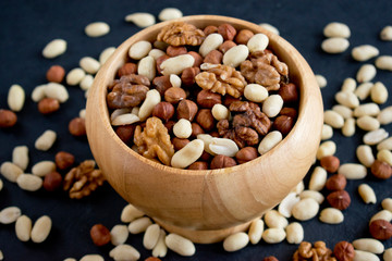 hazelnuts, peanuts, walnuts in wooden bowl on black background