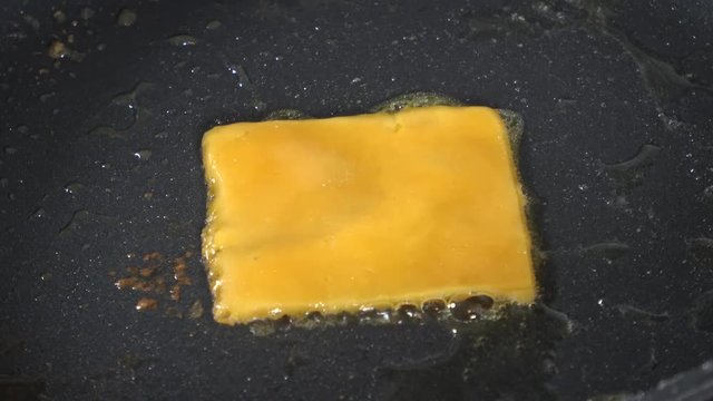 Sliced cheddar melting into a cheese crisp on the stove