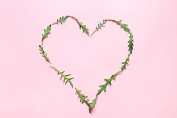 Fototapeta na wymiar Abstract heart shape of arugula on a pink background. Top view. Trendy flat lay for bloggers, designers, magazines etc.