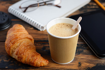 Take away coffee cup with croissant on wooden table.