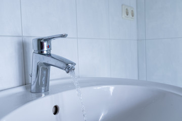 water flowing out of a silver tap at the white sink in bathroom