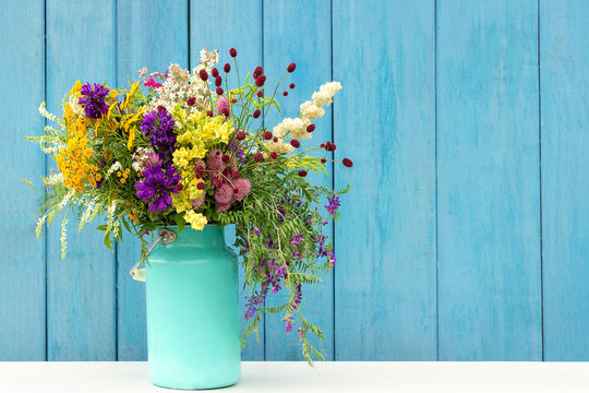 Bouquet of wild flowers in starm tin can vase on background blue wooden boards. Template for postcard Copy space lettering text or design Concept Women's day, Mothers Day, Hello summer or Hello spring