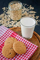 oatmeal cookies with glass of milk on tablecloth and wooden board