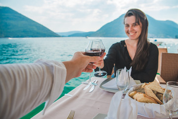 woman with man drinking wine in restaurant at seaside with beautiful view of bay and mountains