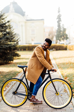 Side view of a young indian hipster man in coat walking with a bicycle on a city street
