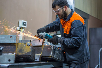 An employee of a machine-building enterprise uses an angle grinder to clean sharp edges.
