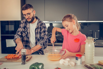 Tall bearded dark-haired man in a checkered shirt cutting sweet pepper