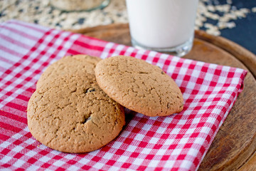 oatmeal cookies with glass of milk on tablecloth and wooden board