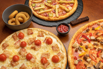 3 different pizzas on the restaurant table with squid and sauce in separate plates