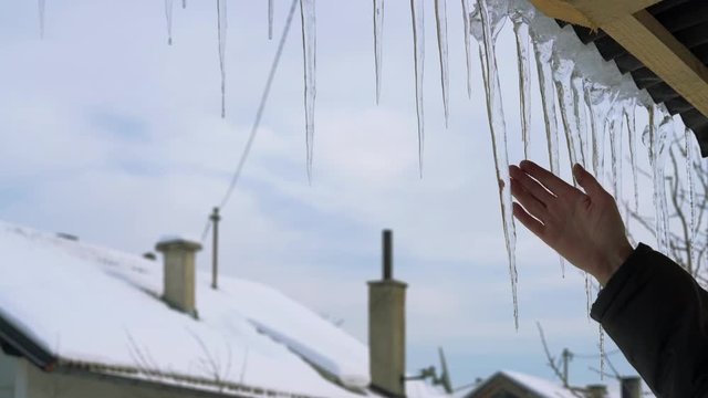 Man touches winter icicles on the roof - (4K)