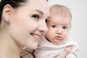 Young woman mother in denim overalls holds a baby child in her arms. White background in the studio.