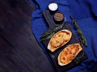 Stuffed eggplant halves roasted with cheese on a black cutting board