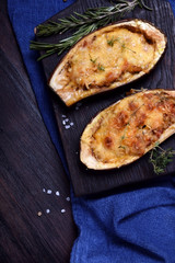 Stuffed eggplant halves roasted with cheese on a black cutting board
