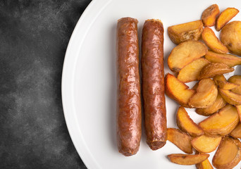beef sausages and fried potatoes on white plate and dark table