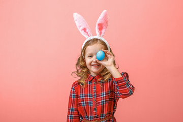 Cheerful little kid girl with bunny ears with an easter egg on a colored background.