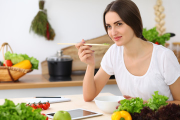 Beautiful Hispanic  woman cooking while using tablet computer in kitchen or  making online shopping by touchpad and credit card. Housewife found new recipe for dinner