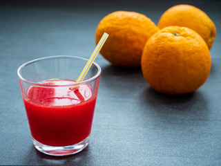 Glas mit Blutorangensaft und Orangen auf dunklem Untergrund