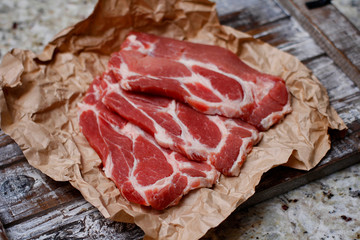 Thinly sliced fresh raw red meat on craft cooking paper on wooden table.