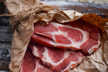 Thinly sliced fresh raw red meat on craft cooking paper on wooden table.