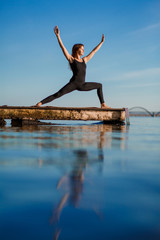 Fototapeta na wymiar Young woman practicing yoga exercise at quiet wooden pier with city background. Sport and recreation in city rush