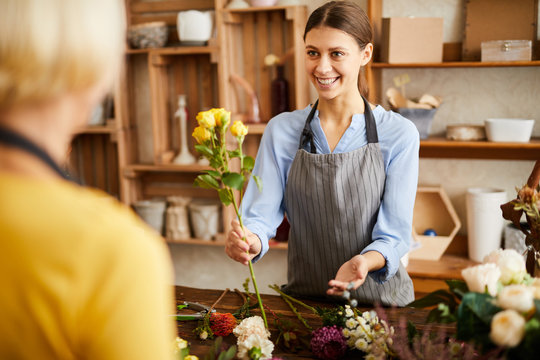 Waist up portrait of smiling young woman selling flowers to client while working in flower shop, copy space