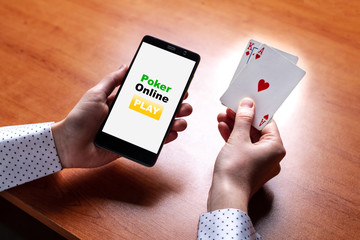 Close up of poker player with playing cards and smartphone in hands at the table. Online poker and gambling. Mobile poker app
