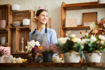 Waist up portrait of smiling young woman looking away while working in flower shop, copy space - obrazy, fototapety, plakaty