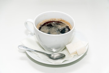 Cup of black coffee on a saucer with a napkin, a teaspoon and lumps of sugar
