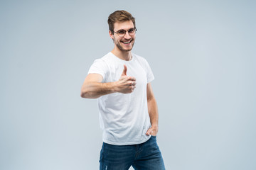 Image of attractive man showing thumb up on camera with happy smile isolated over gray background.