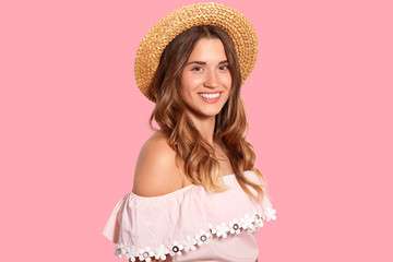 Studio shot of attractive woman with joyful expression, stands sideways at camera, has healthy...