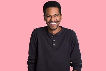 Photo of pleased joyful dark skinned man laughs positively, has broad smile, hears funny story or joke, wears casual clothes, isolated over pink background, feels optimistic and satisfied. Emotions