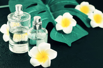 Perfume spray bottles on black table with green plant decor leaf and tropical flowers, spa & massage background. 

