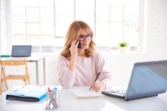 Businesswoman talking with somebody and working on laptop in the office